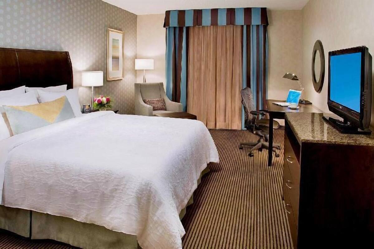 Una habitación de hotel con una cama grande, un escritorio con computadora, televisor y una silla.