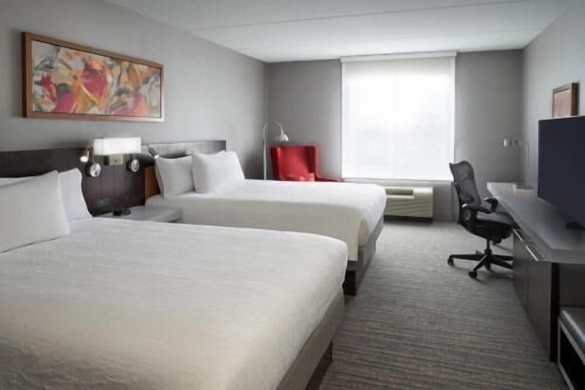 Une chambre d’hôtel avec deux lits, un bureau, une chaise, une télévision et une fenêtre avec des rideaux.