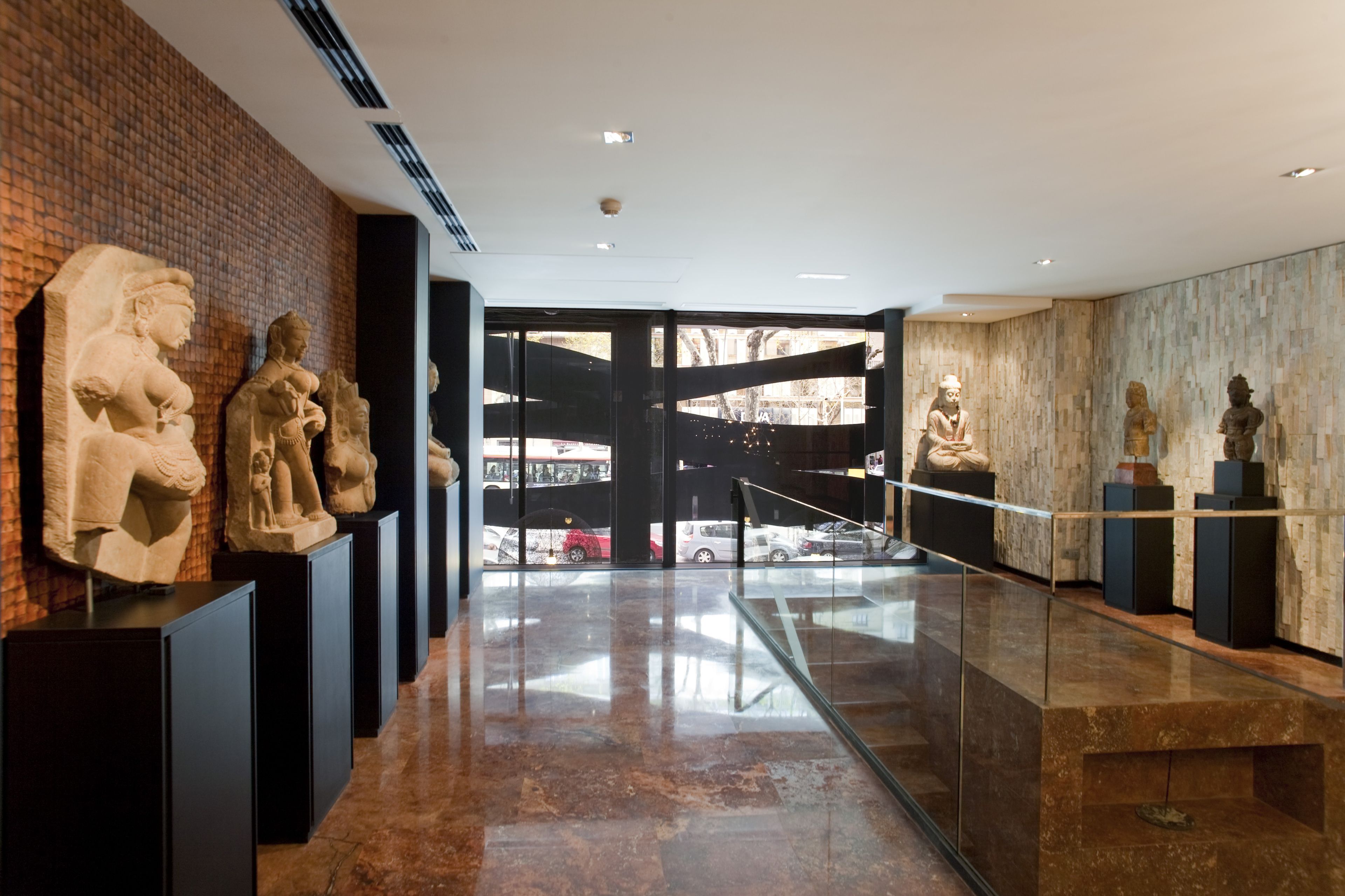 Un interior moderno con barandilla de vidrio, esculturas de piedra y pared de ladrillo.