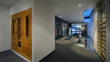 Un pasillo moderno de hotel con un ascensor de madera, una pared de vidrio que ofrece vistas a la ciudad y un área de fitness con equipo de ejercicio.