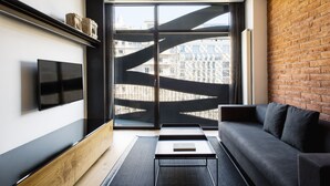 Una sala de estar moderna con un sofá negro, un televisor de pantalla plana y un ventanal con vistas a edificios.
