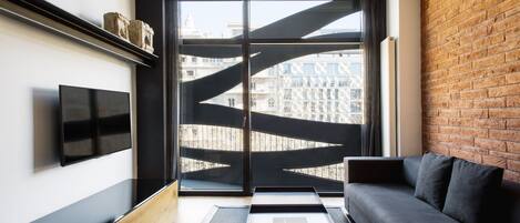 Un soggiorno moderno con un divano nero, una TV a schermo piatto e una grande finestra vista edifici.