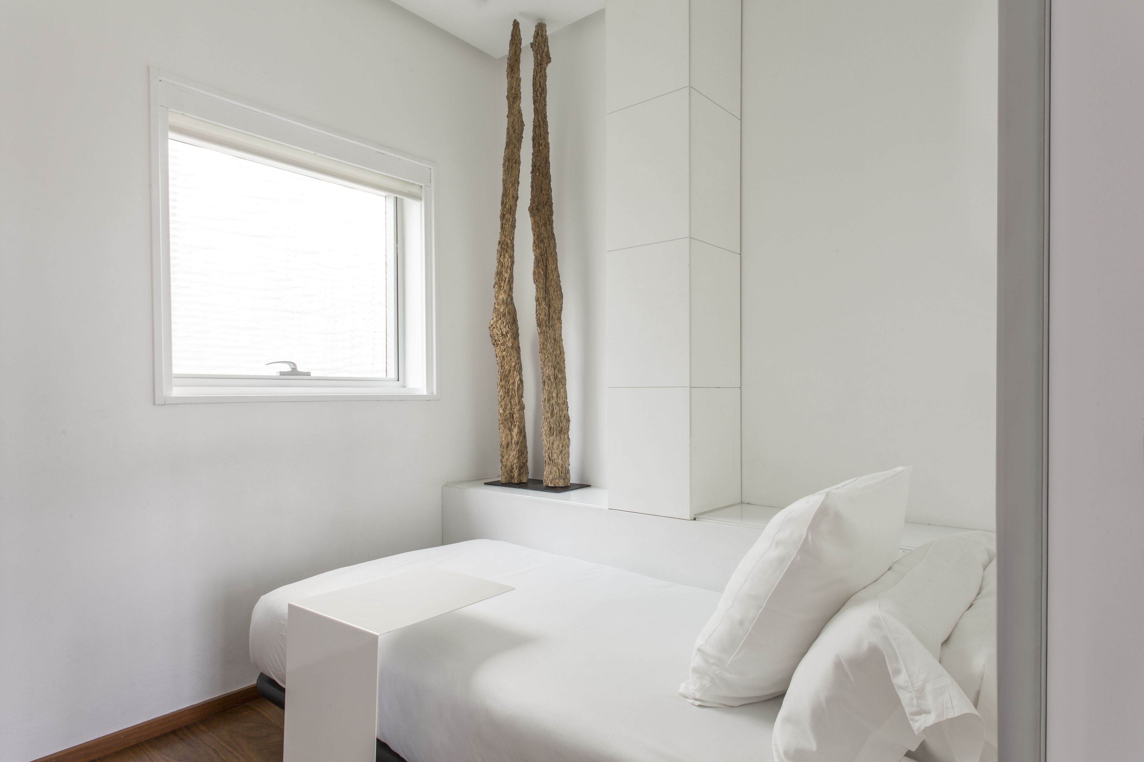 A minimalist bedroom with a bed, a window, and a tall decorative piece.