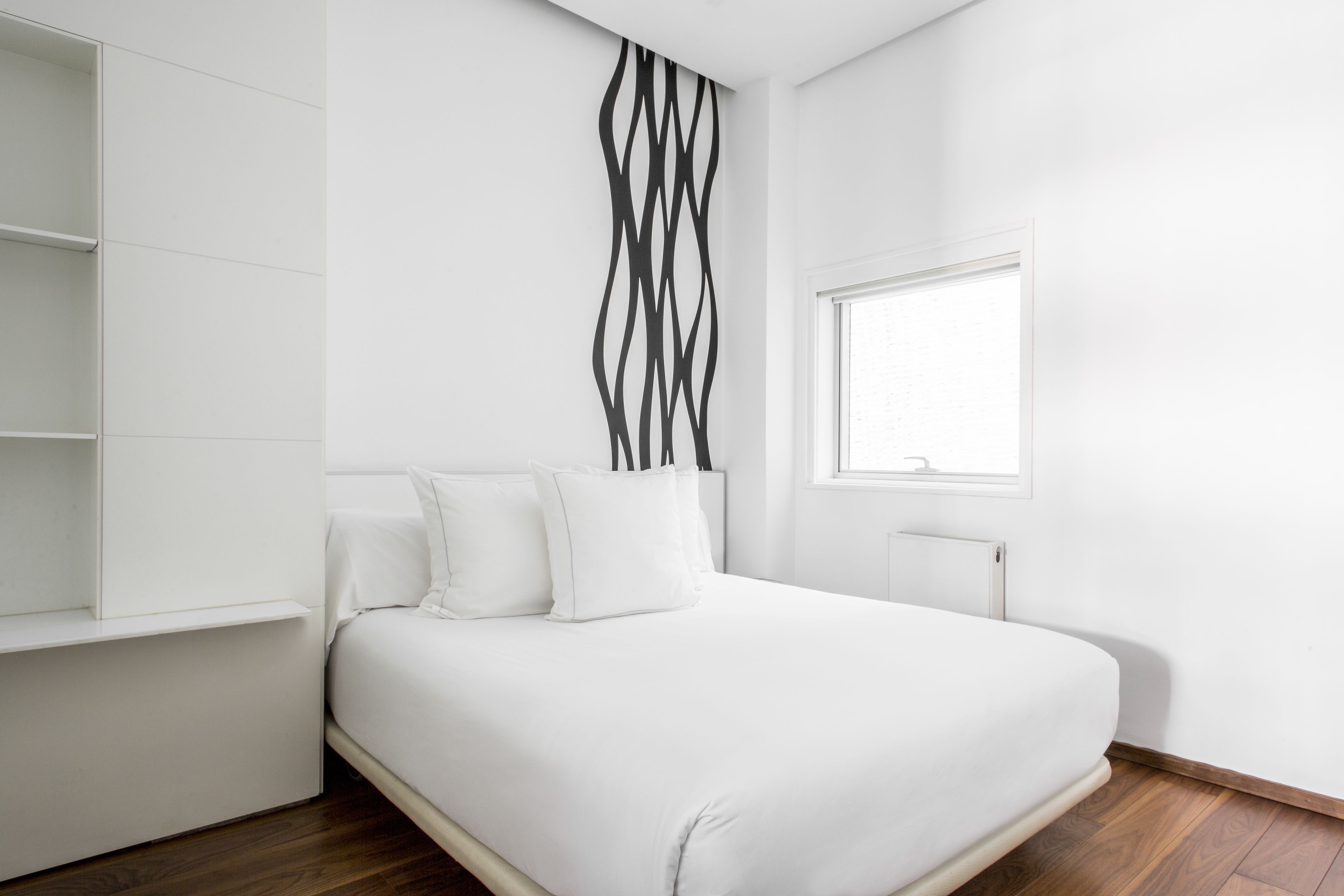 A modern bedroom with a bed, white walls, a window, and a radiator.