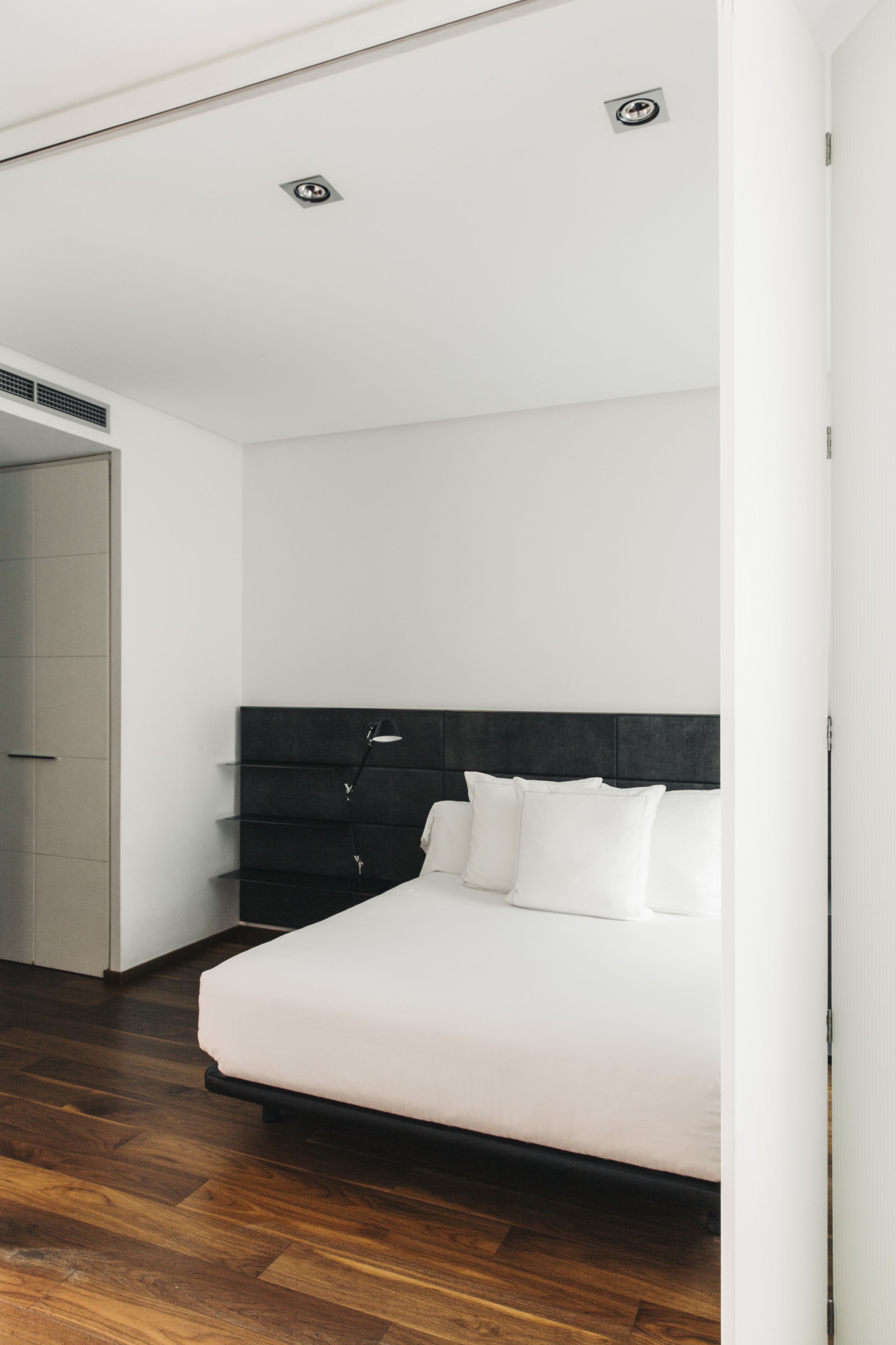 A modern bedroom with a large bed, a dark headboard, and a white wall.