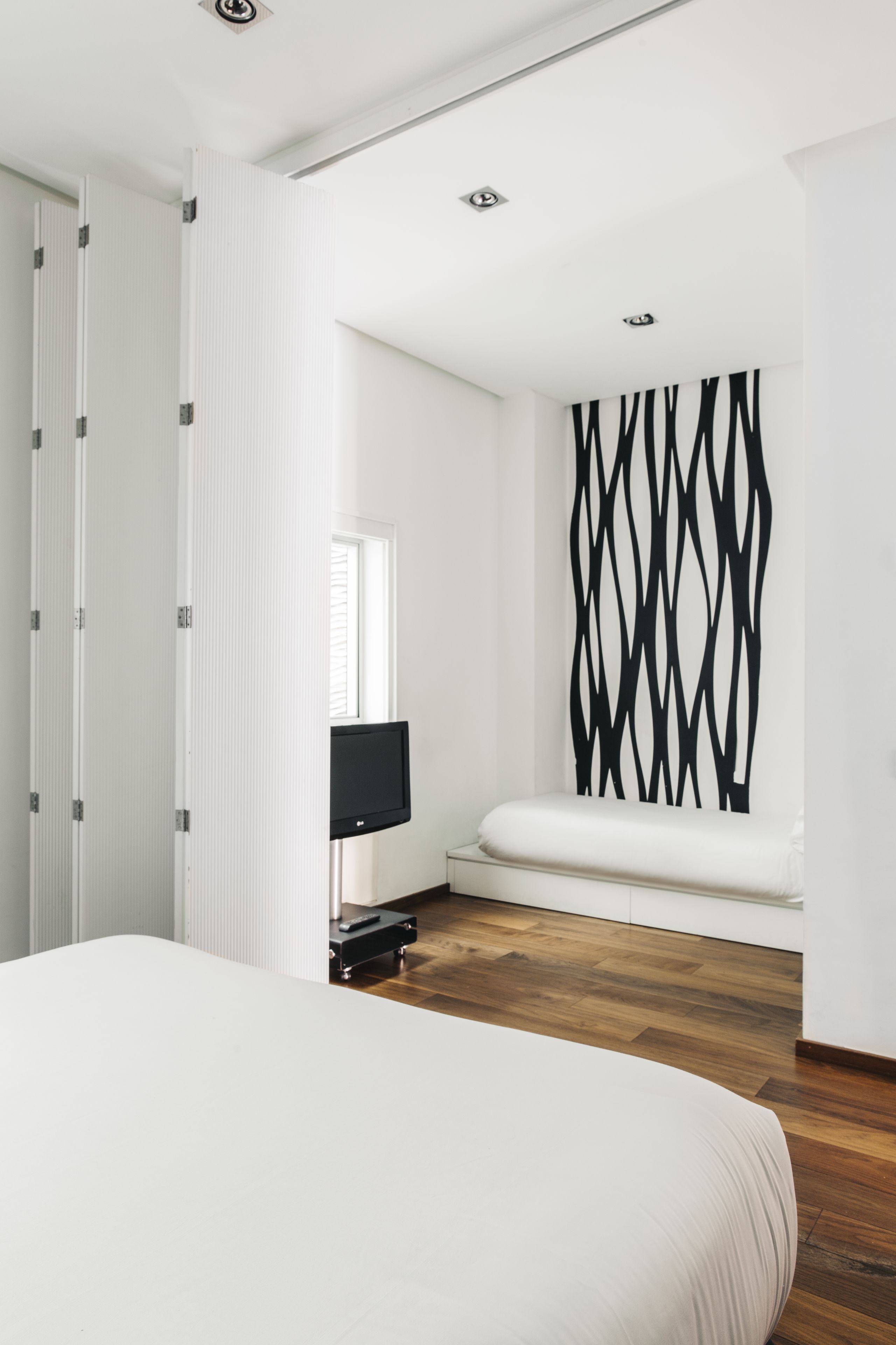 A modern bedroom with a large bed, a television, and a unique black and white wall art.