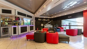 A modern bar lounge with a piano, red and black seating, and a bar area with bottles and glasses. - Au Grand Hôtel de Sarlat (Sarlat-la-Canéda)