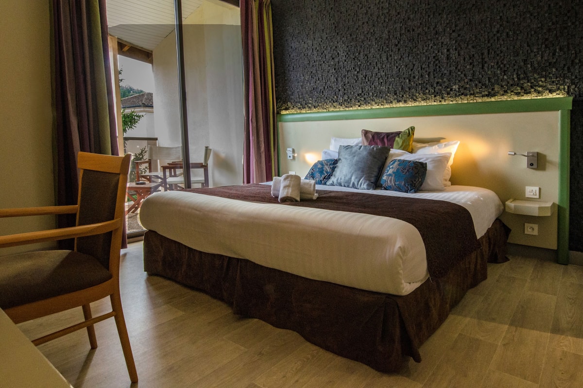 A hotel room with a large bed, a wooden chair, a green headboard, and a view of the outdoors.