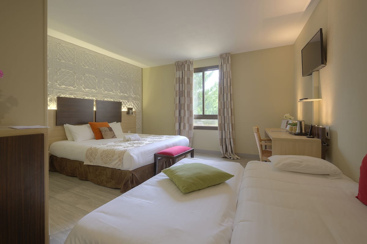 A hotel room with two beds, a desk, a chair, a TV, and a window with curtains.
