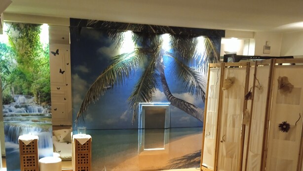 A bedroom with a bed, a nightstand, a lamp, and a wall mural of a beach scene. - Au Grand Hôtel de Sarlat (Sarlat-la-Canéda)