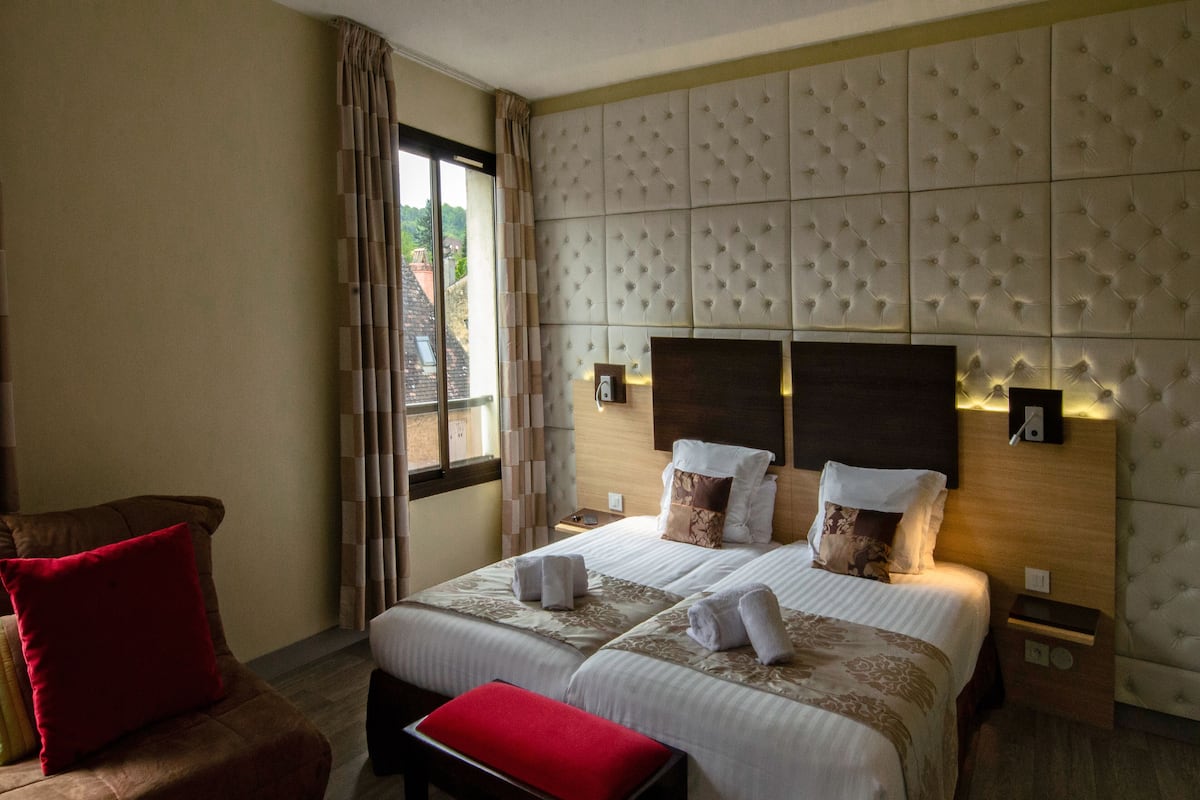 A hotel room with a large bed, two bedside tables, a red chair, and a window with curtains.
