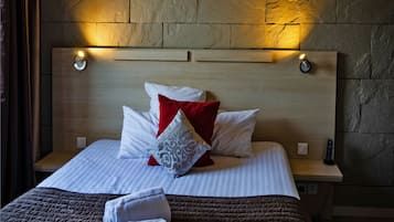 A neatly made bed with a brown quilt, white pillows, and a red pillow. There are two bedside lamps on the nightstands.