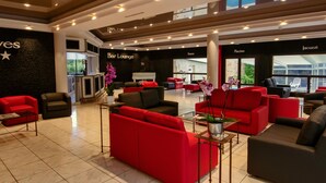 A hotel lobby with red and black sofas, a bar lounge, and a view of the outdoors. - Au Grand Hôtel de Sarlat (Sarlat-la-Canéda)