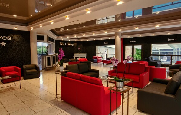 Un hall de hotel con sofás rojo y negro, un bar lounge y vistas al exterior.