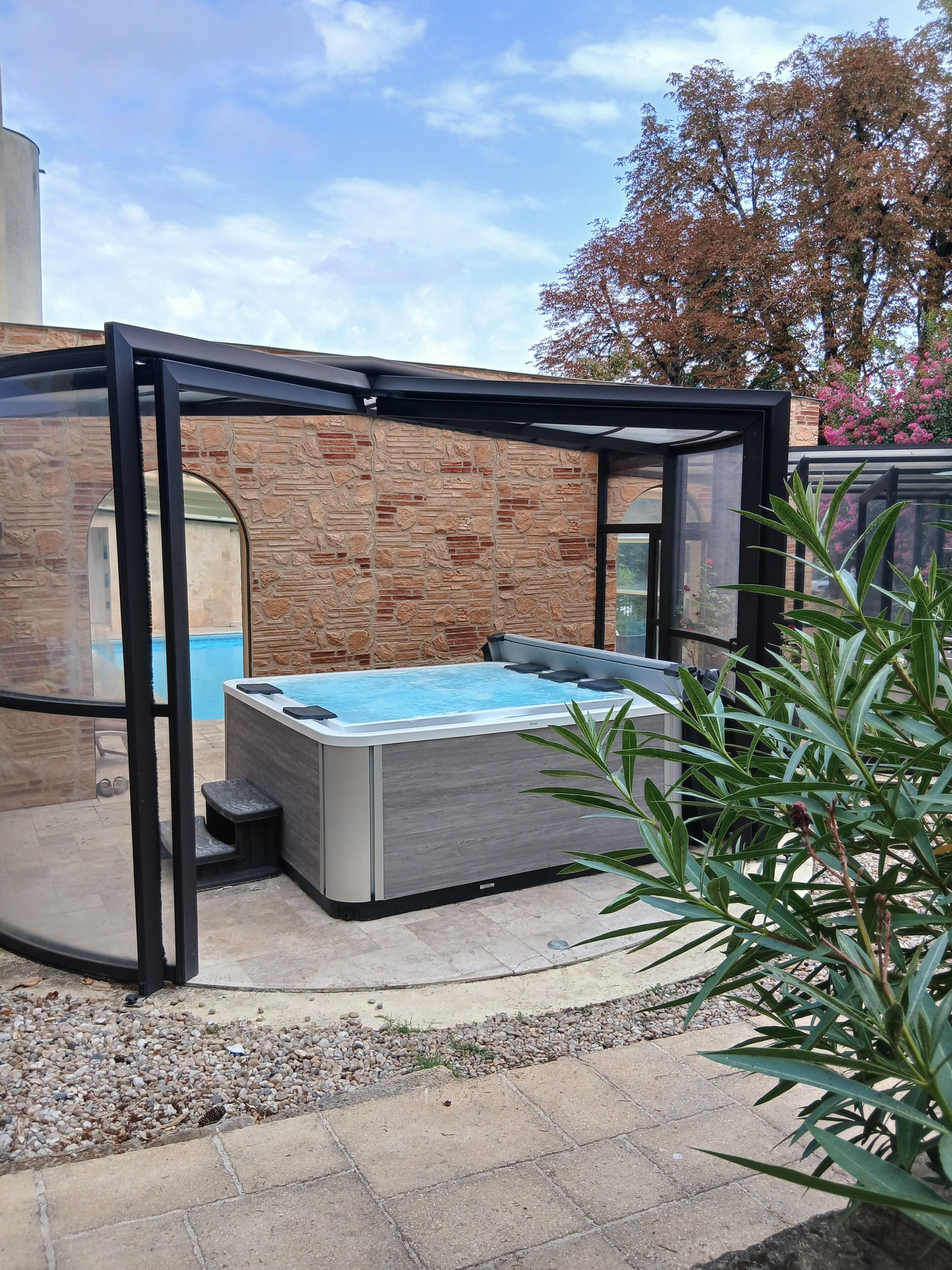 A hot tub in a covered outdoor area with a brick wall and glass enclosure.