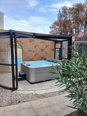 A hot tub in a covered outdoor area with a brick wall and glass enclosure. - Au Grand Hôtel de Sarlat (Sarlat-la-Canéda)