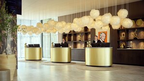 A reception area with three gold reception desks, a large chandelier, and a wall with decorative items and a framed picture. - Van Der Valk Hotel Amersfoort A1 (Amersfoort)