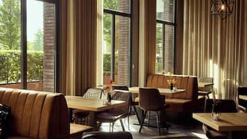 Een modern restaurant met grote ramen, leren zitplaatsen en een geometrisch lichtarmatuur.