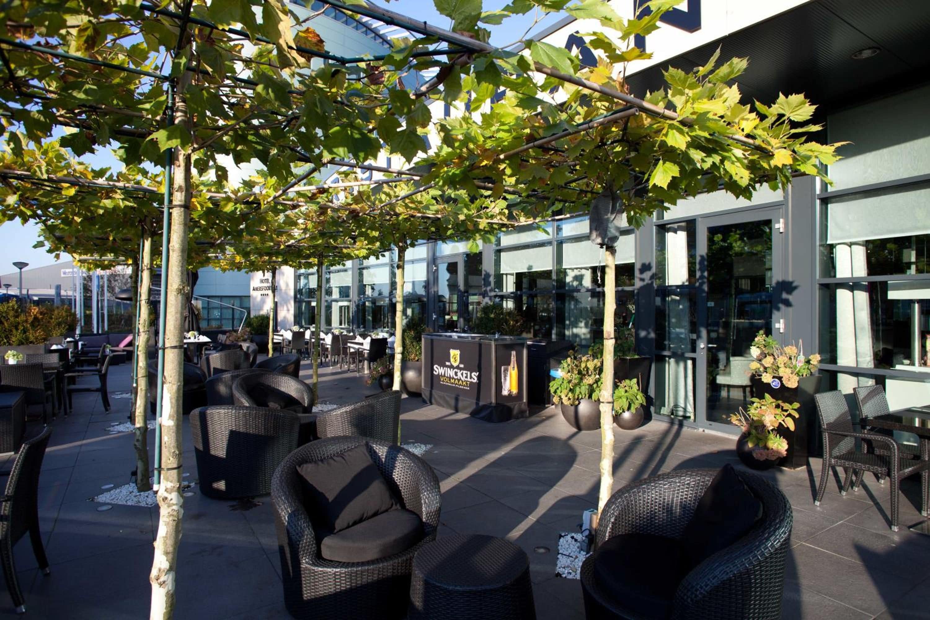 An outdoor seating area with wicker furniture, a bar area, and a building with large windows.
