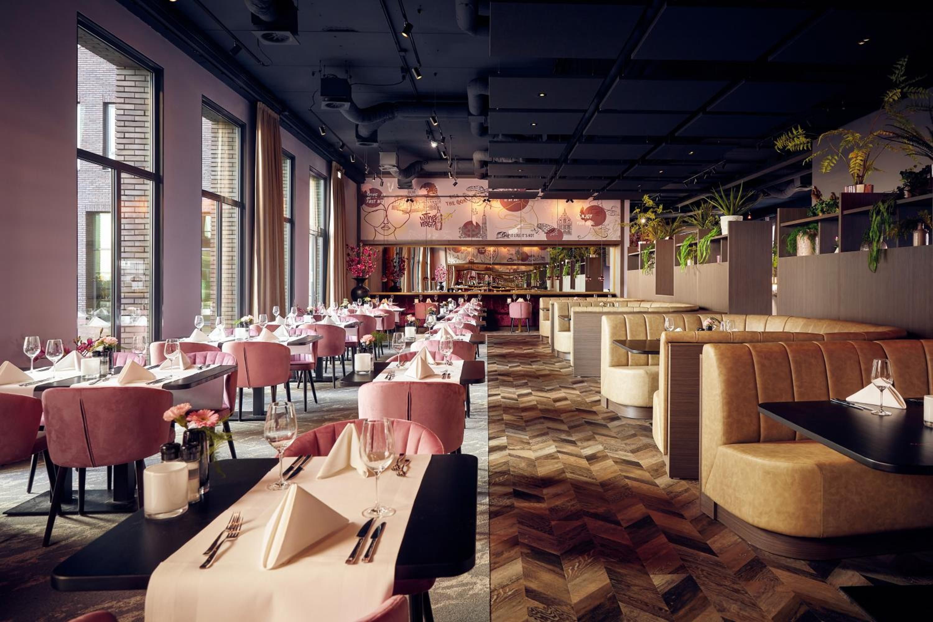 Um restaurante com várias mesas e cabines, janelas amplas e um chão com padrão herringbone.