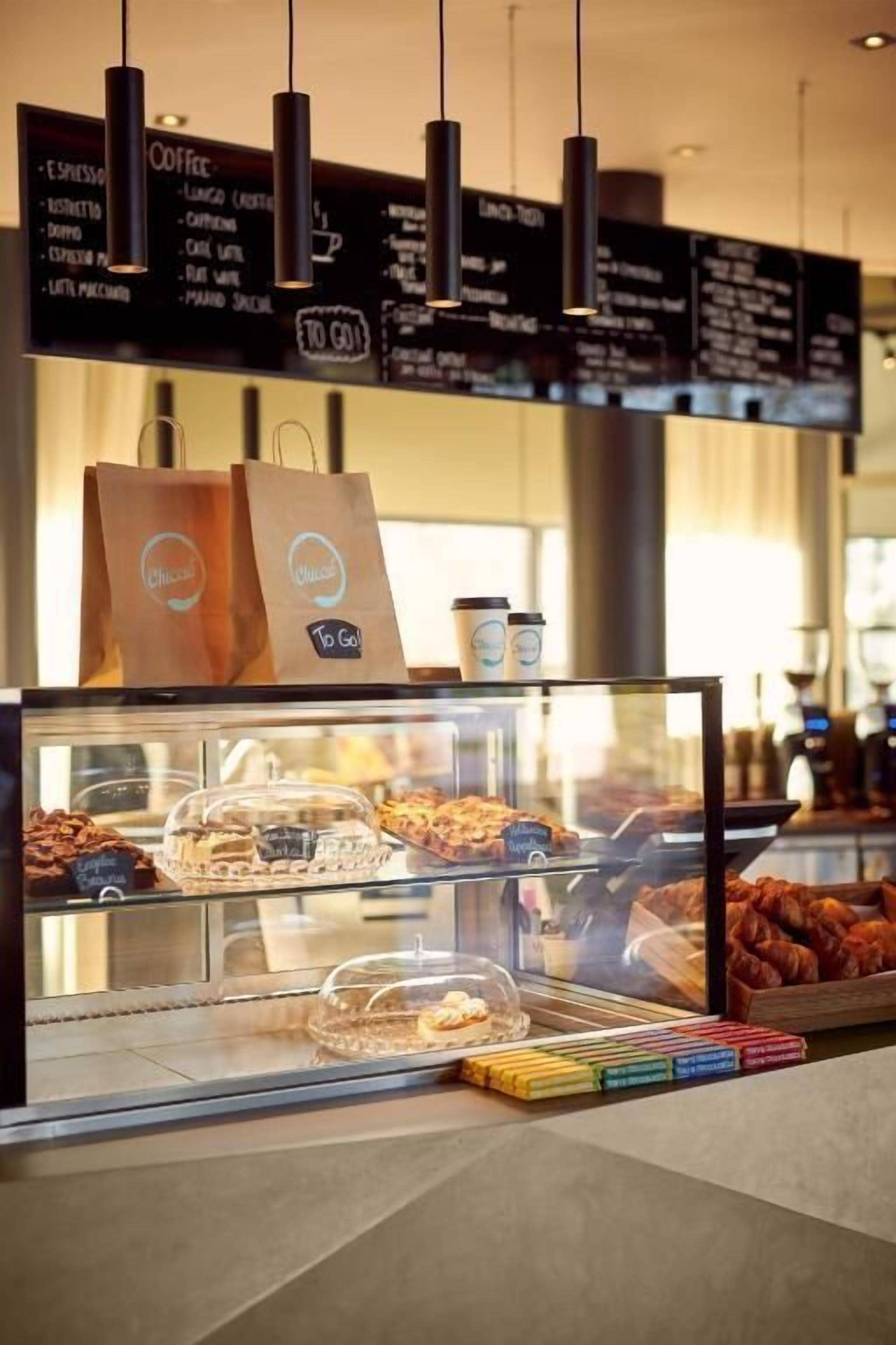 Una cafetería con un menú en la pizarra, una vitrina de pasteles y una bolsa para llevar.