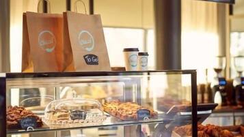 Una cafetería con un menú en la pizarra, una vitrina de pasteles y una bolsa para llevar.
