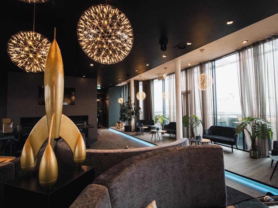 Un hall d’hôtel moderne avec un comptoir d’accueil, un espace salon et de grandes fenêtres.