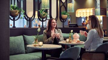 Two people seated at a table with a green sofa and a small round table in a cozy indoor setting.