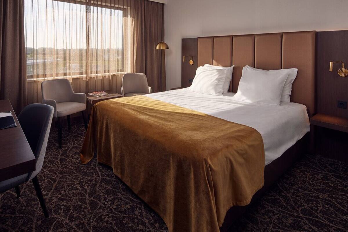 A hotel room with a large bed, a desk, a chair, and a window with curtains.