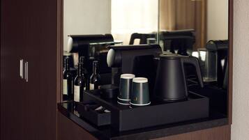 A minibar with a coffee maker, wine bottles, and coffee cups.