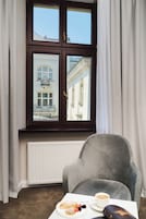 A room with a window, a radiator, a grey armchair, a table with a plate of food and a cup of coffee.