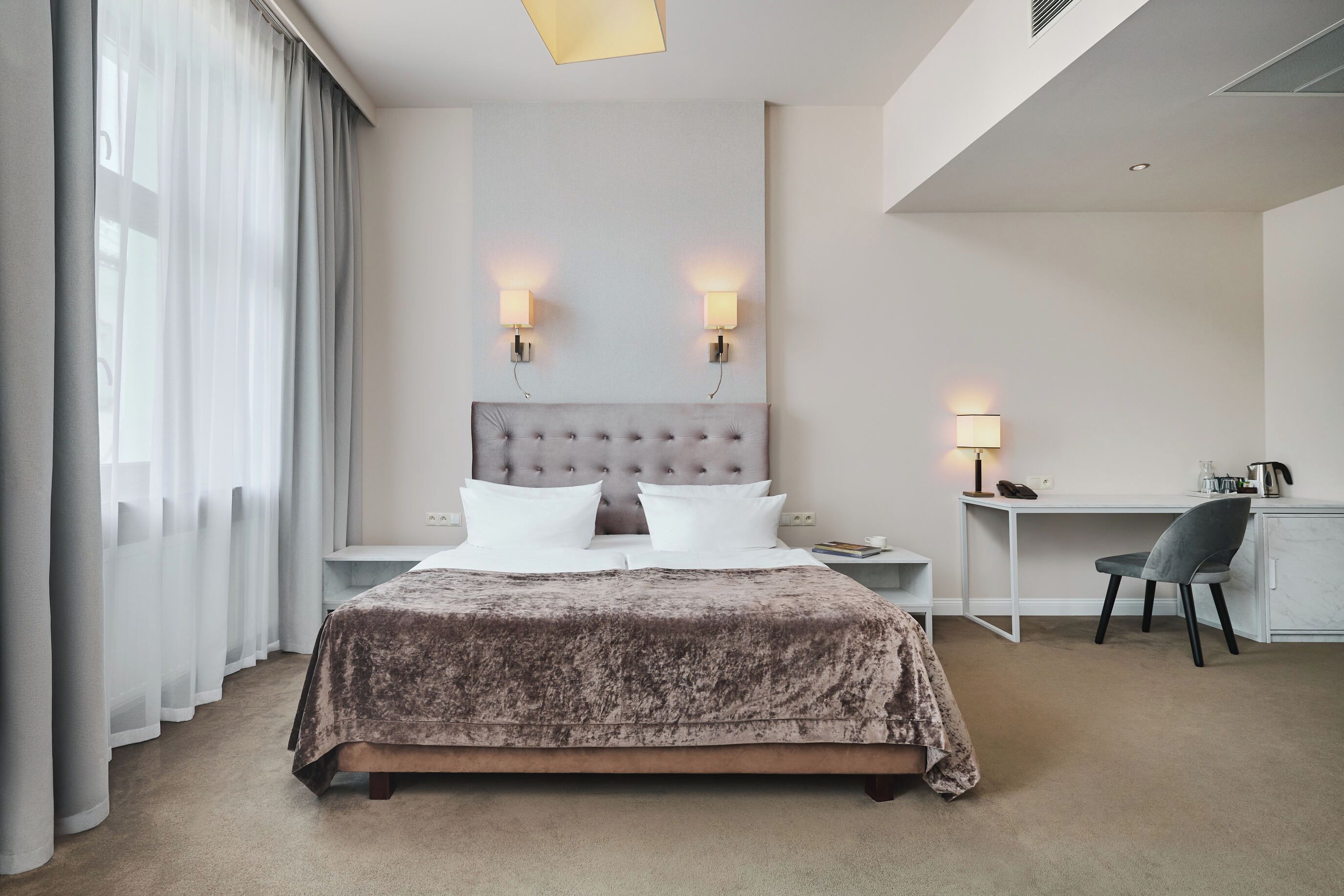 Een hotelkamer met een groot bed, twee bedlampen, een bureau met stoel en uitzicht op het omliggende landschap.