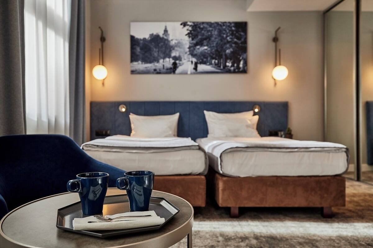 A hotel room with two beds, a round table with a tray, and a painting on the wall.
