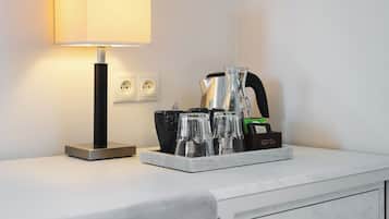 A hotel room with a bedside table, a lamp, a kettle, and a tray with glasses and a coffee maker.