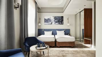 A hotel room with two beds, a blue chair, a small table with a tray of items, and a large window with curtains.