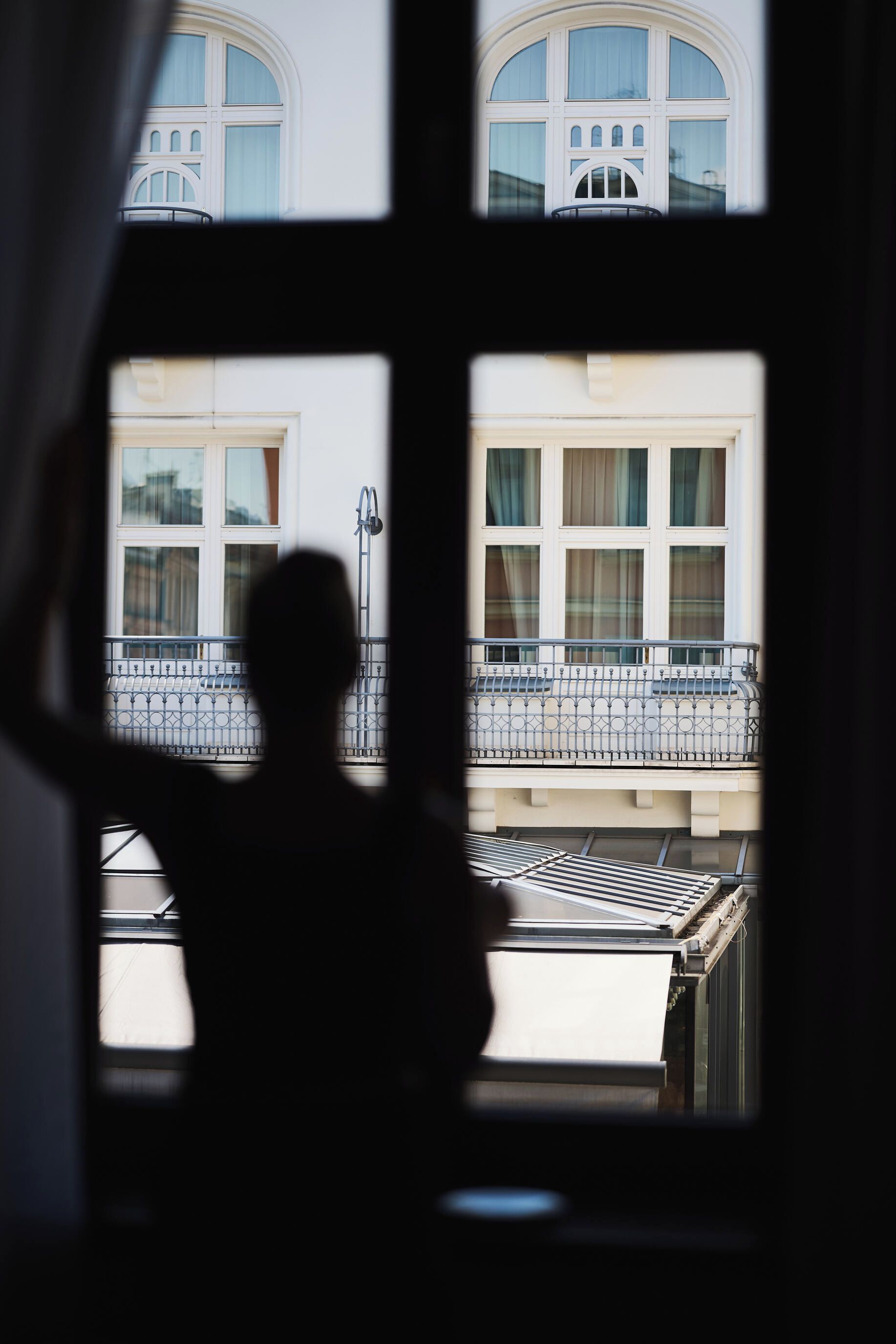 Silueta de una persona frente a un ventanal con vistas a un edificio con múltiples ventanas y balcones.