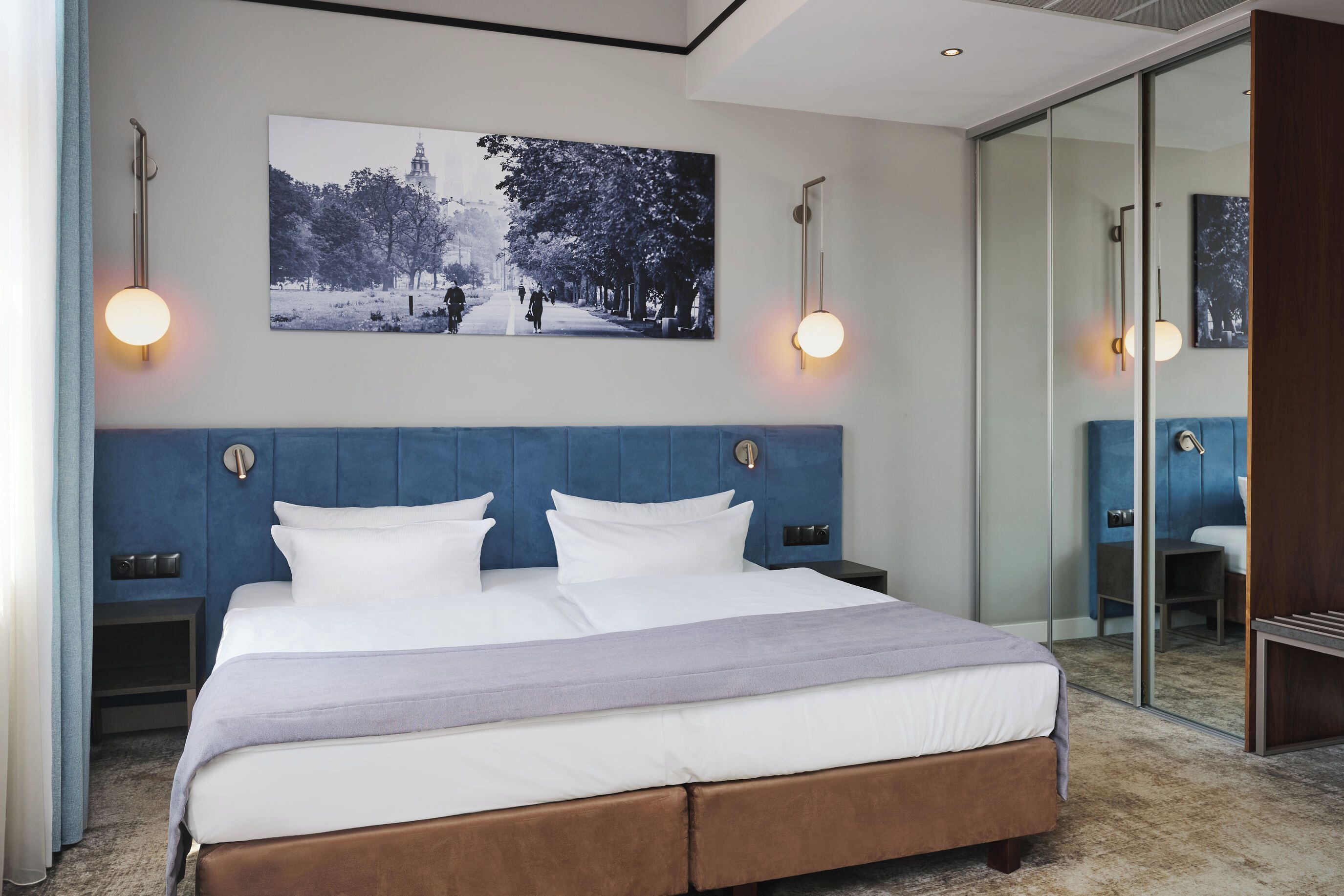 A modern hotel room with a large bed, a wall-mounted picture, and a glass partition.