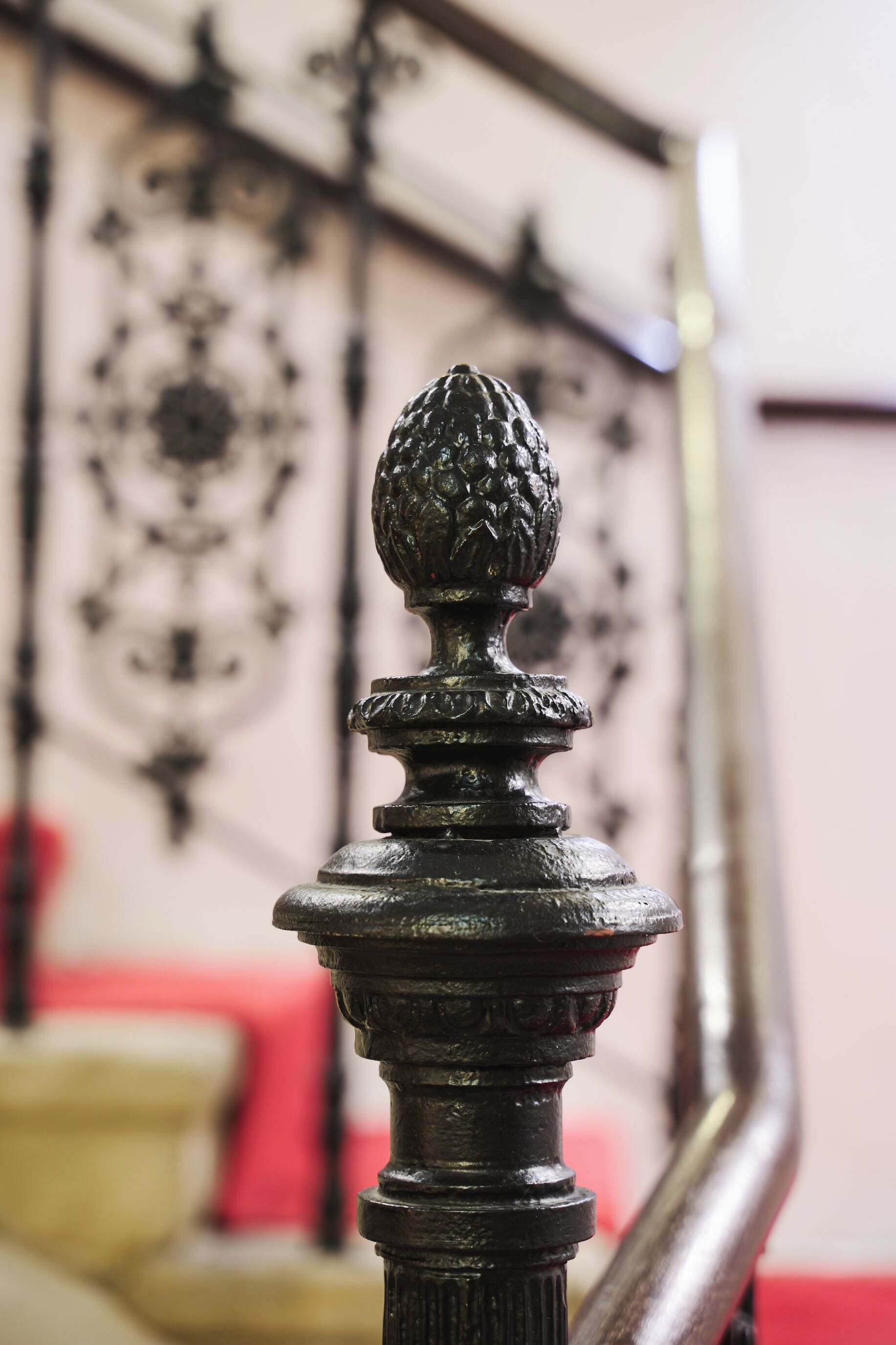 A close-up of a decorative metal balustrade with a spherical finial, set against a background with a patterned metal design and a red cushion.