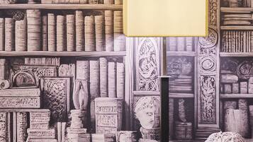A room with a bookshelf filled with books and decorative items, a lamp, and a bust sculpture.