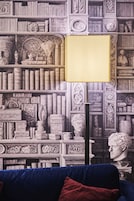 Una habitación con una estantería llena de libros y objetos decorativos, una lámpara y un busto.