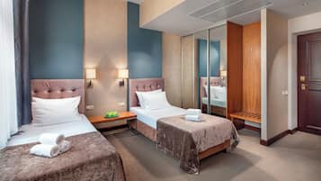 Quarto de hotel com duas camas, um guarda-roupa, um espelho e uma mesa de cabeceira com abajur.