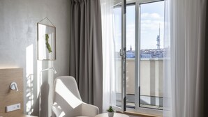 A modern hotel room with a large sliding glass door to a balcony, a comfortable chair, a small table with a plant, and a minimalist decor. - Botanique Hotel Prague (Prague)