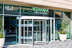 Un bâtiment moderne avec une entrée en verre et une enseigne indiquant : « HÔTEL BOTANIQUE – BAR-BISTROT ».