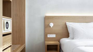 A neatly organized hotel room with a wooden headboard, a bedside table with a lamp, and a built-in safe.