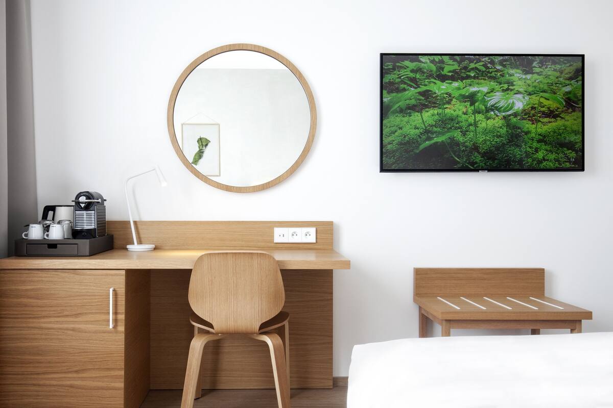 A hotel room with a wooden desk, a chair, a bed, a TV, and a mirror.