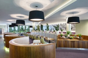 Restaurante moderno com móveis de madeira, luminárias pendentes pretas e plantas em vasos.