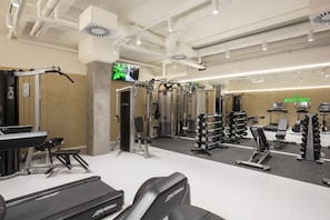 Une salle de sport équipée de divers appareils d’exercice, notamment des tapis de course, des appareils de musculation et des poids libres.