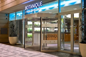 Exterior do Botanique Hotel Bistro Bar, com entrada em vidro e grandes vasos de plantas.