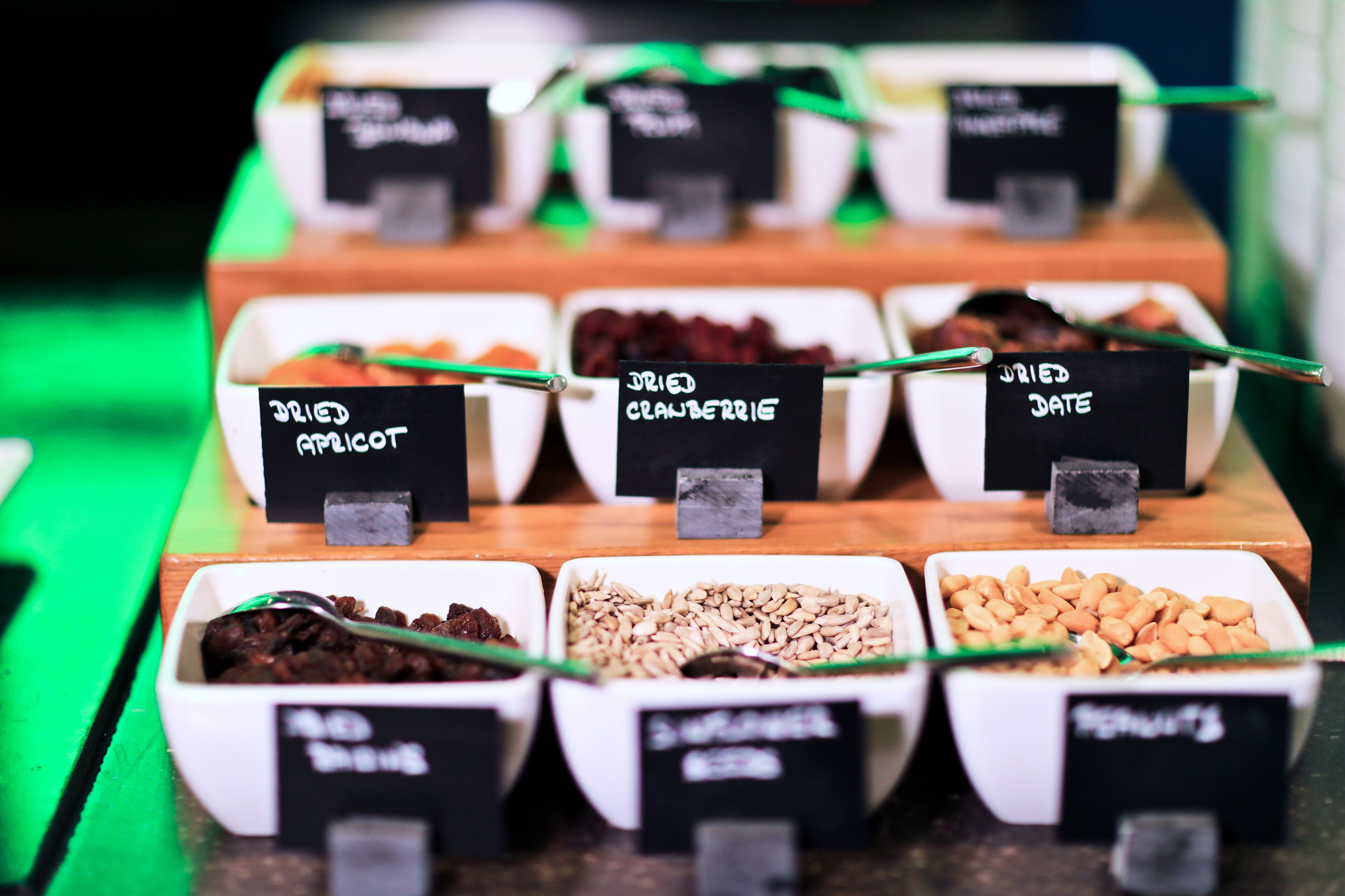 A display of various dried fruits and nuts, including dried apricots, cranberries, dates, and almonds, arranged in white containers with black labels.