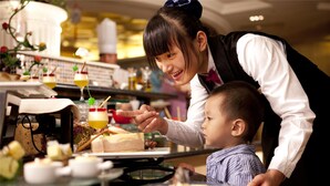 A woman serving food to a child at a table with various dishes and drinks. - Chateau Star River (Beijing)